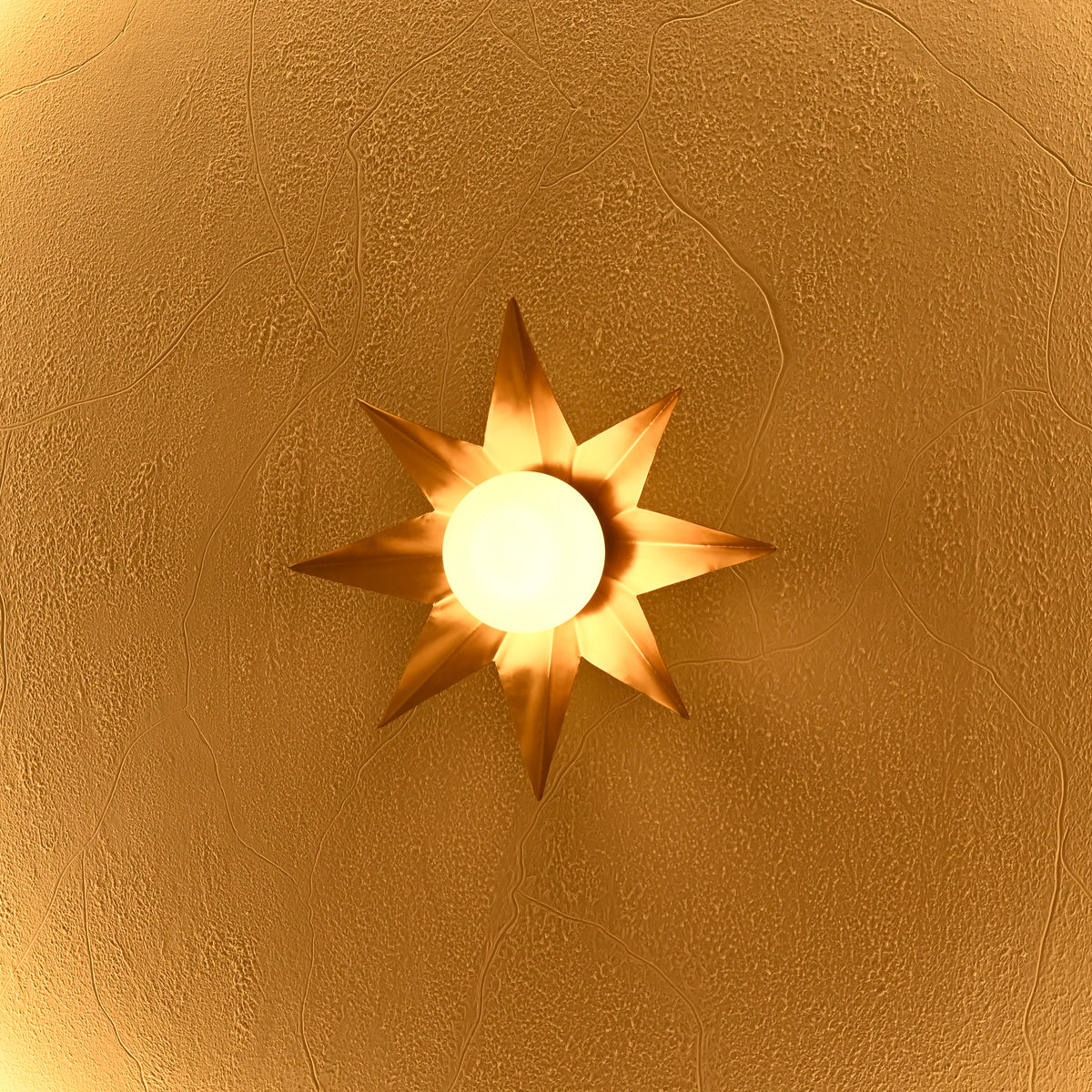Detailed view of gold starburst wall light showing sculptural pointed rays and softly illuminated central white globe.
