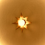 Detailed view of gold starburst wall light showing sculptural pointed rays and softly illuminated central white globe.