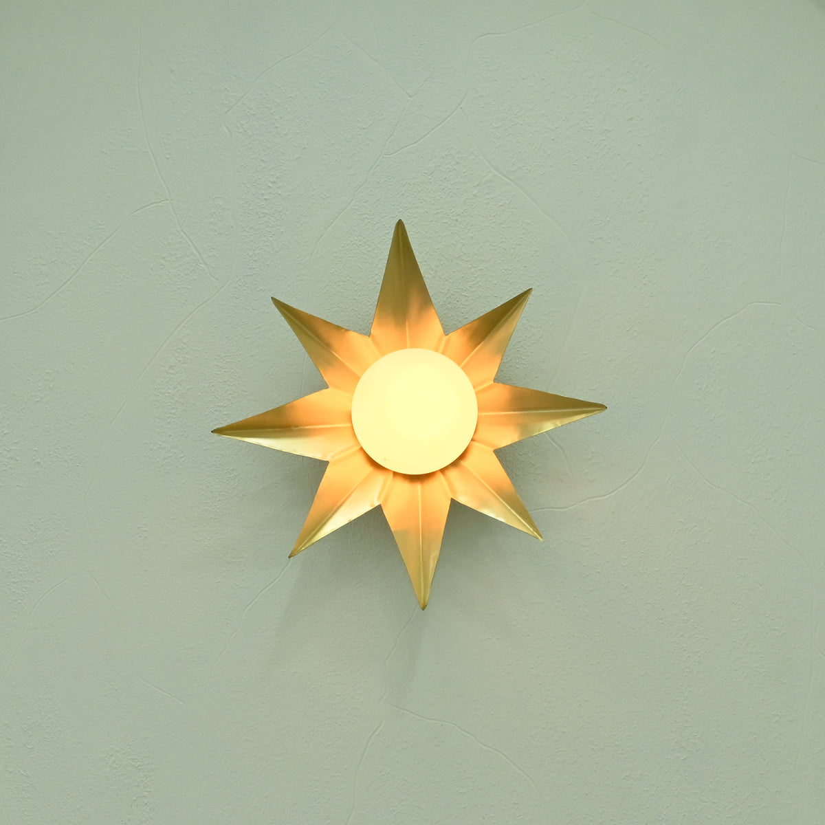 Close-up of illuminated gold starburst wall sconce with frosted globe diffuser and warm golden reflections on a textured wall.