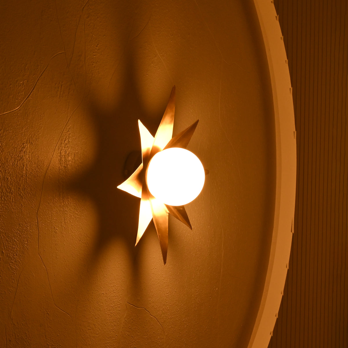 Side angle of gold starburst wall sconce highlighting its projecting frosted globe and dimensional metal star design.