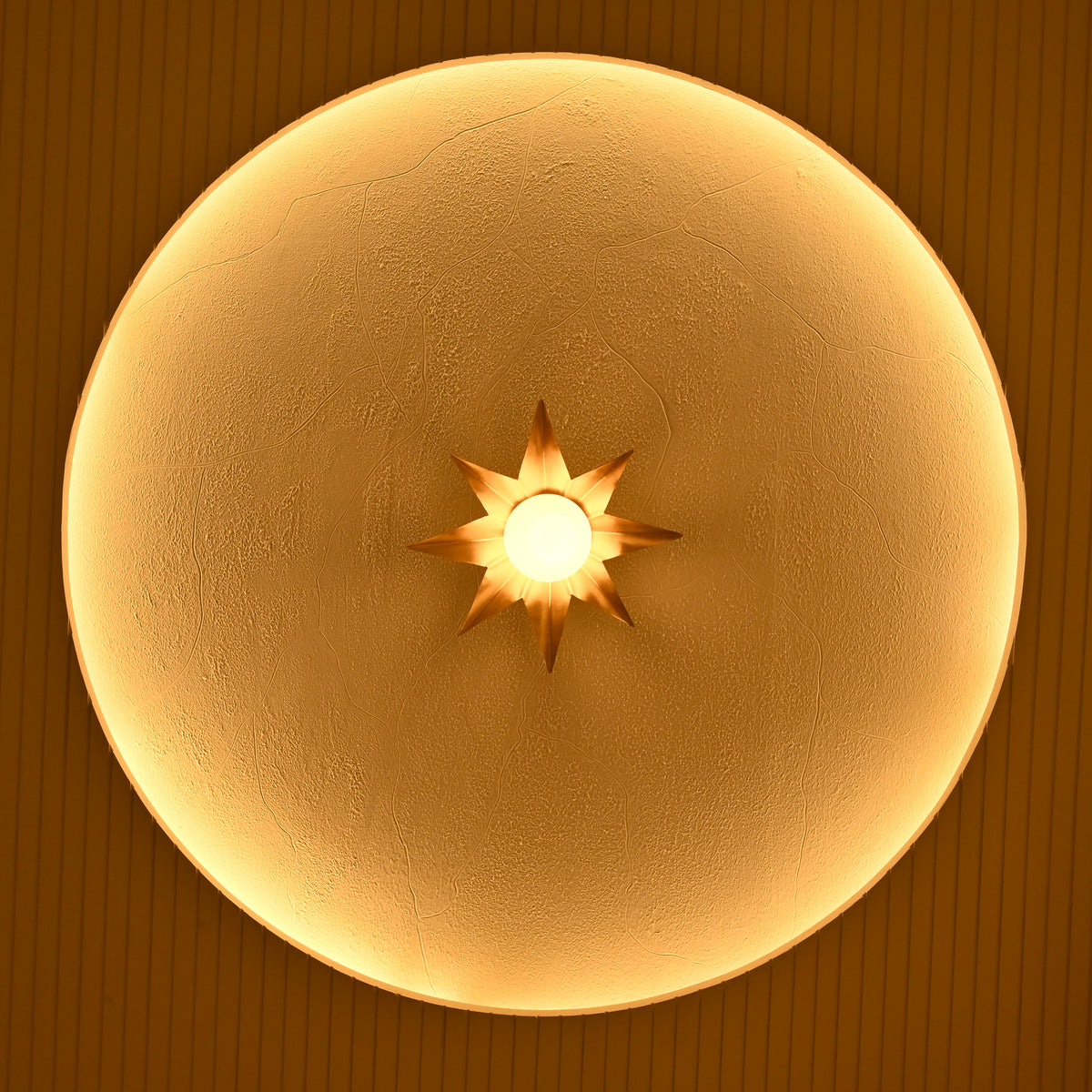 Gold eight-point starburst wall sconce glowing warmly inside a circular architectural wall niche with textured finish.