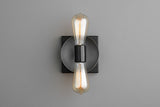 Modern wall sconce with dark graphite round disc on black square backplate and two vertical Edison filament bulbs, minimalist wall lighting.