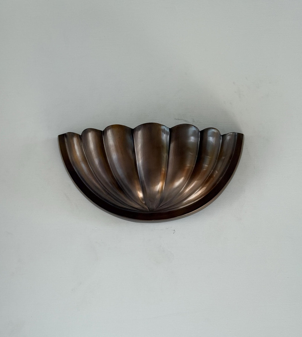 Half-flower fluted brass wall sconce uplight in warm bronze finish shown mounted on a light wall, wider room-view framing.