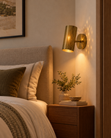 Hobart brass perforated cylinder wall sconce installed beside an upholstered bedroom headboard above a wooden nightstand, creating warm bedside lighting.