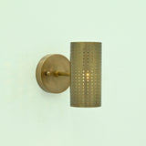  Hobart single-light antique brass wall sconce with illuminated perforated cylindrical metal shade and round mounting backplate.