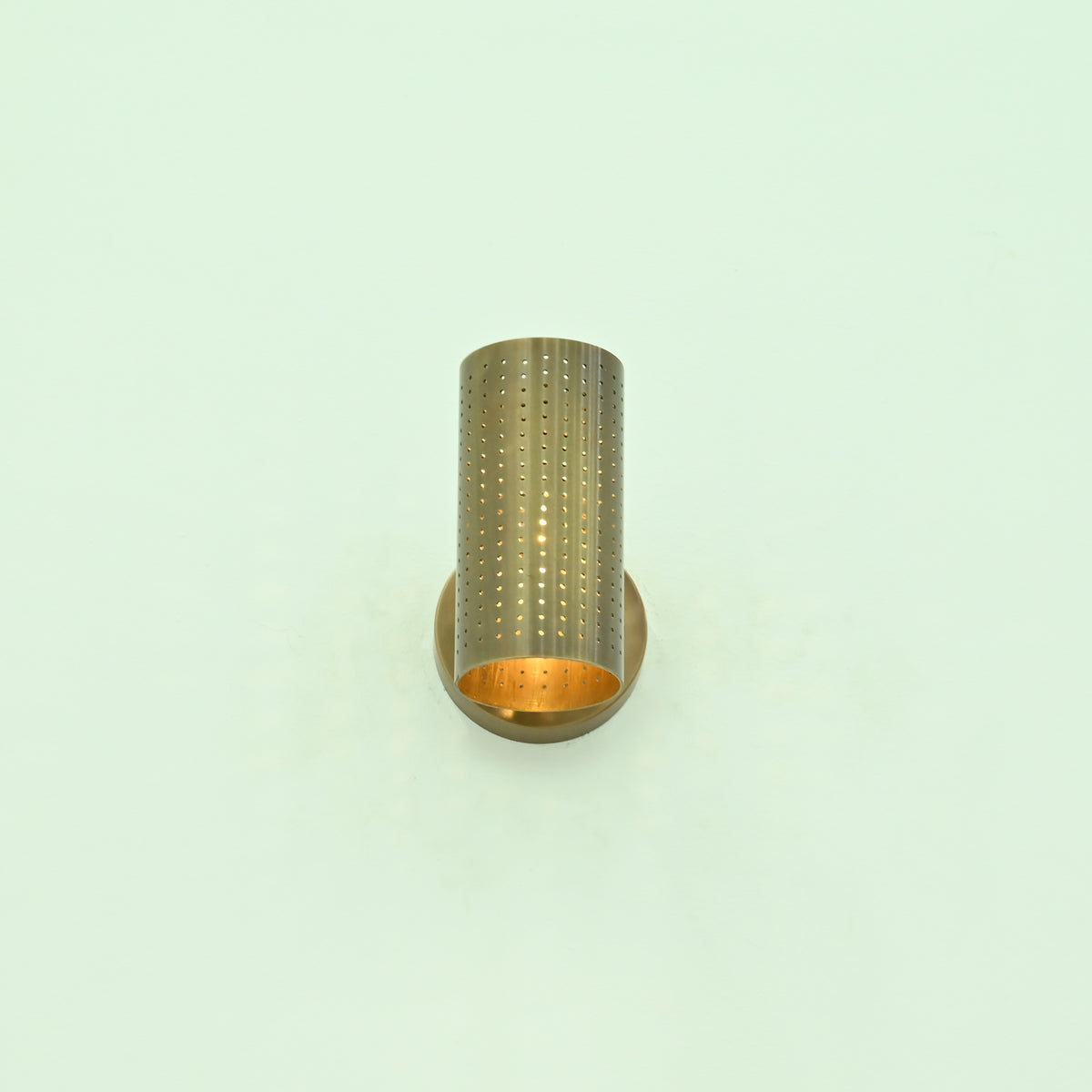 Bottom angled view of Hobart brass wall sconce showing open cylindrical shade, perforated metal detailing, and warm interior illumination.