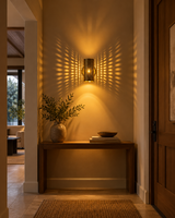 Hobart antique brass perforated cylinder wall sconce illuminating a modern entryway with warm patterned lighting above a wooden console table.