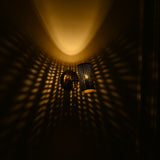 Hobart angled brass cylinder wall sconce projecting golden perforated light patterns and a soft downward beam against a dark wall.