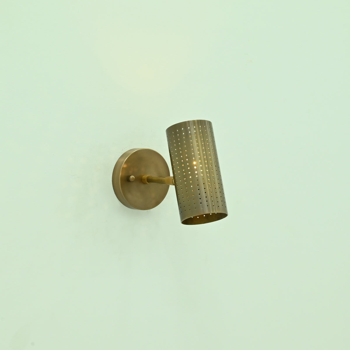 Hobart antique brass wall sconce featuring an angled perforated cylindrical shade, slim support arm, and round metal wall mount.