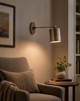 Hudson adjustable cylinder wall sconce installed beside a living room armchair, providing warm directional accent lighting in a modern Scandinavian-inspired interior.