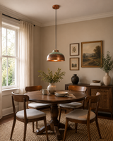 Hudson aged copper dome pendant light installed above a round dining table in a warm contemporary dining room, showcasing its handcrafted copper shade and rustic industrial style.