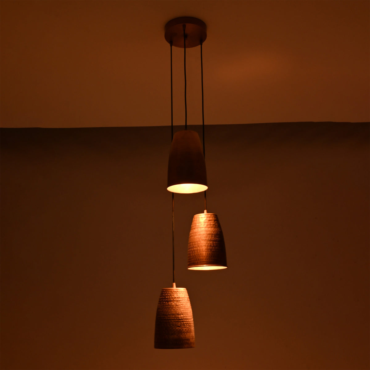 Evening view of the Hudson Cascading Cone Cluster Pendant Light with softly illuminated handcrafted copper cone shades creating a cozy atmosphere.