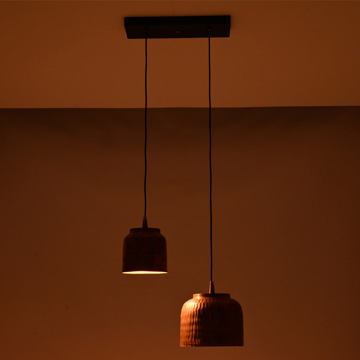 Ambient night view of Hudson hammered copper dual pendant chandelier with staggered pendant shades creating warm focused illumination.