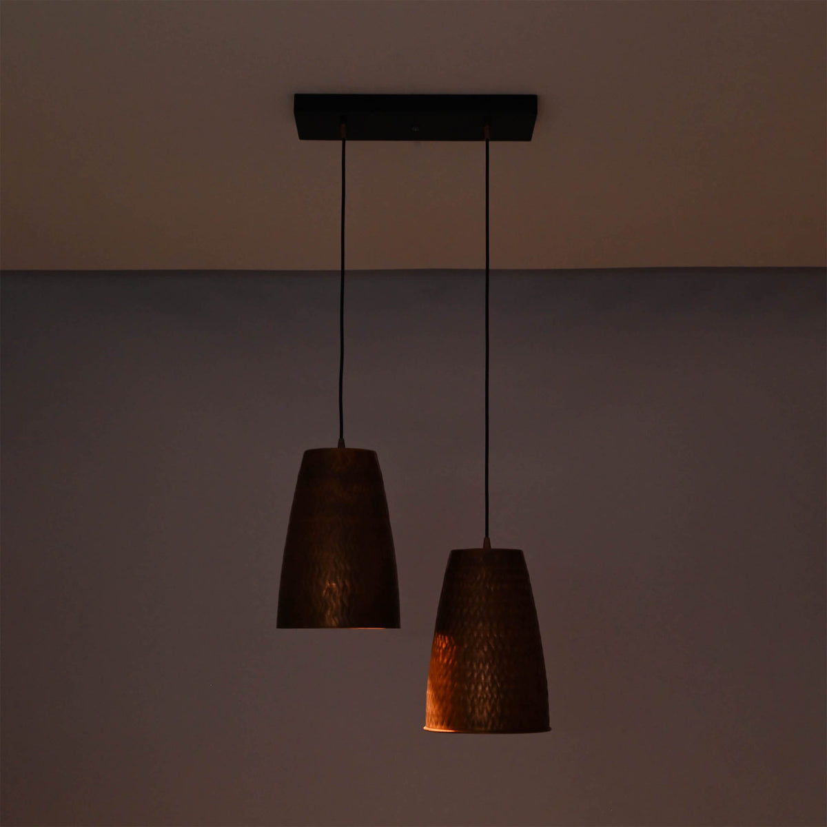 Hudson handcrafted copper dual cone pendant light illuminated with warm ambient lighting highlighting the textured metal finish.