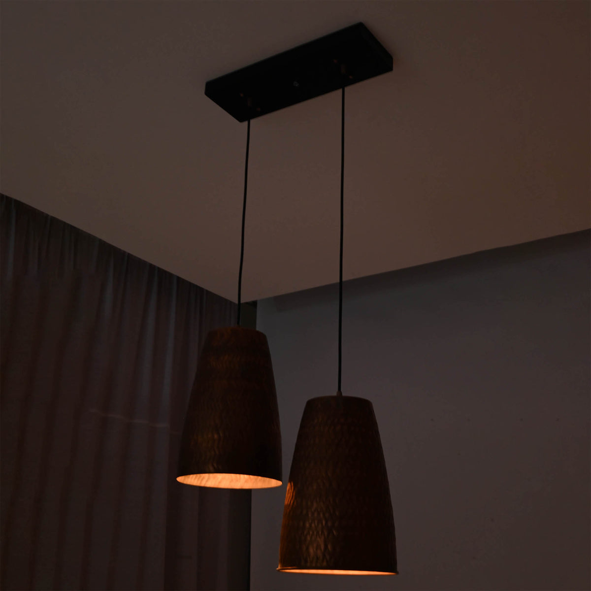 Hudson handcrafted copper dual cone pendant light displayed in a dark interior with warm focused illumination from textured metal shades.