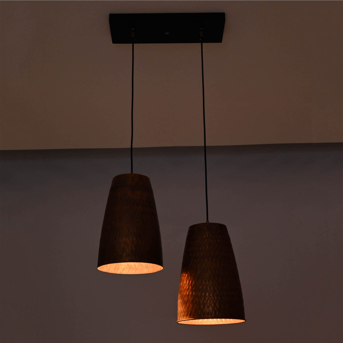 Warm illuminated Hudson Modern Artisan pendant light with handcrafted copper cone shades creating soft downward lighting.
