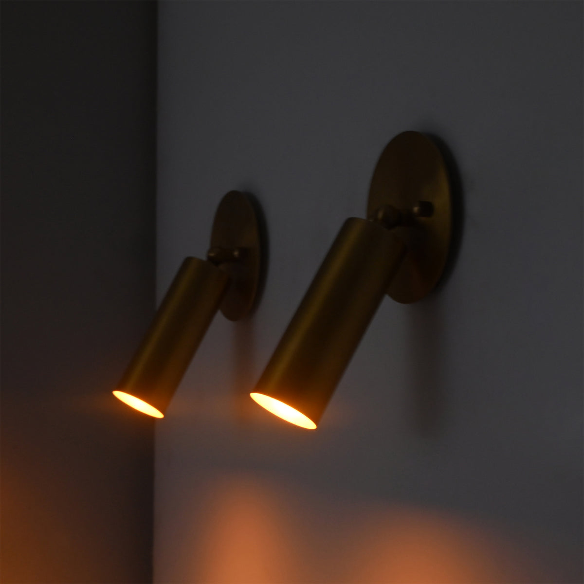 Close-up of two Hudson Modern Brass Adjustable Cylinder Wall Sconces casting warm focused beams to demonstrate their directional task and accent lighting performance.
