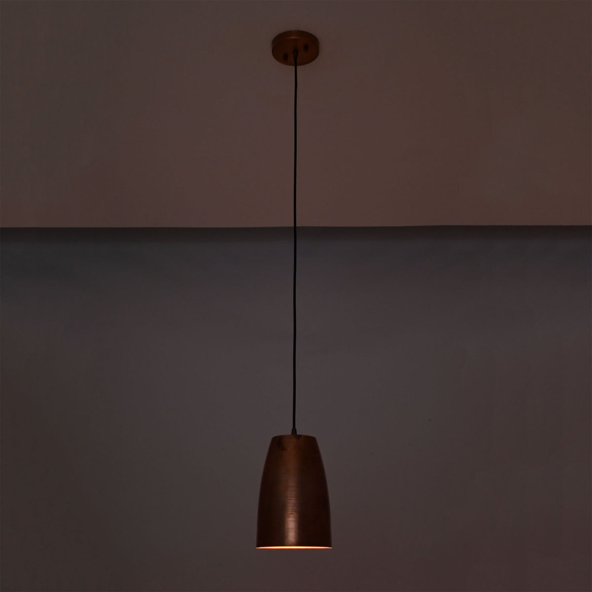 Hudson brushed copper bell pendant light illuminated with warm downward lighting in a dark setting