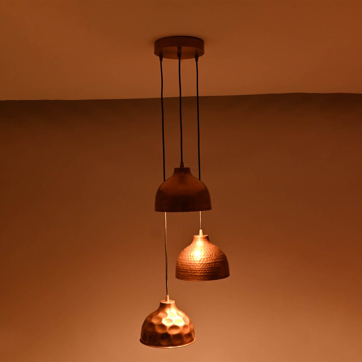 Warm illuminated view of Hudson modern copper three shade cluster pendant light with artisan copper dome shades