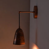 Side view of the Hudson Modern Hammered Copper Cone Wall Sconce installed on a wall, casting a warm downward light that highlights its handcrafted hammered copper shade.