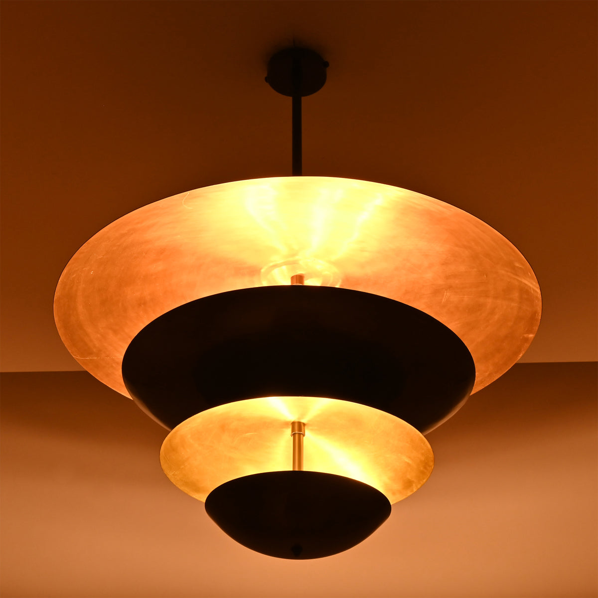 Hudson Modern Layered Disc Chandelier producing soft ambient illumination through layered black metal shades with warm metallic reflective interiors.