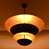 Hudson Modern Layered Disc Chandelier producing soft ambient illumination through layered black metal shades with warm metallic reflective interiors.