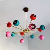 Hudson 12 light multicolor chandelier shown from a sculptural angled view with vibrant pink, turquoise, and red shades arranged around a brass-tone central hub.
