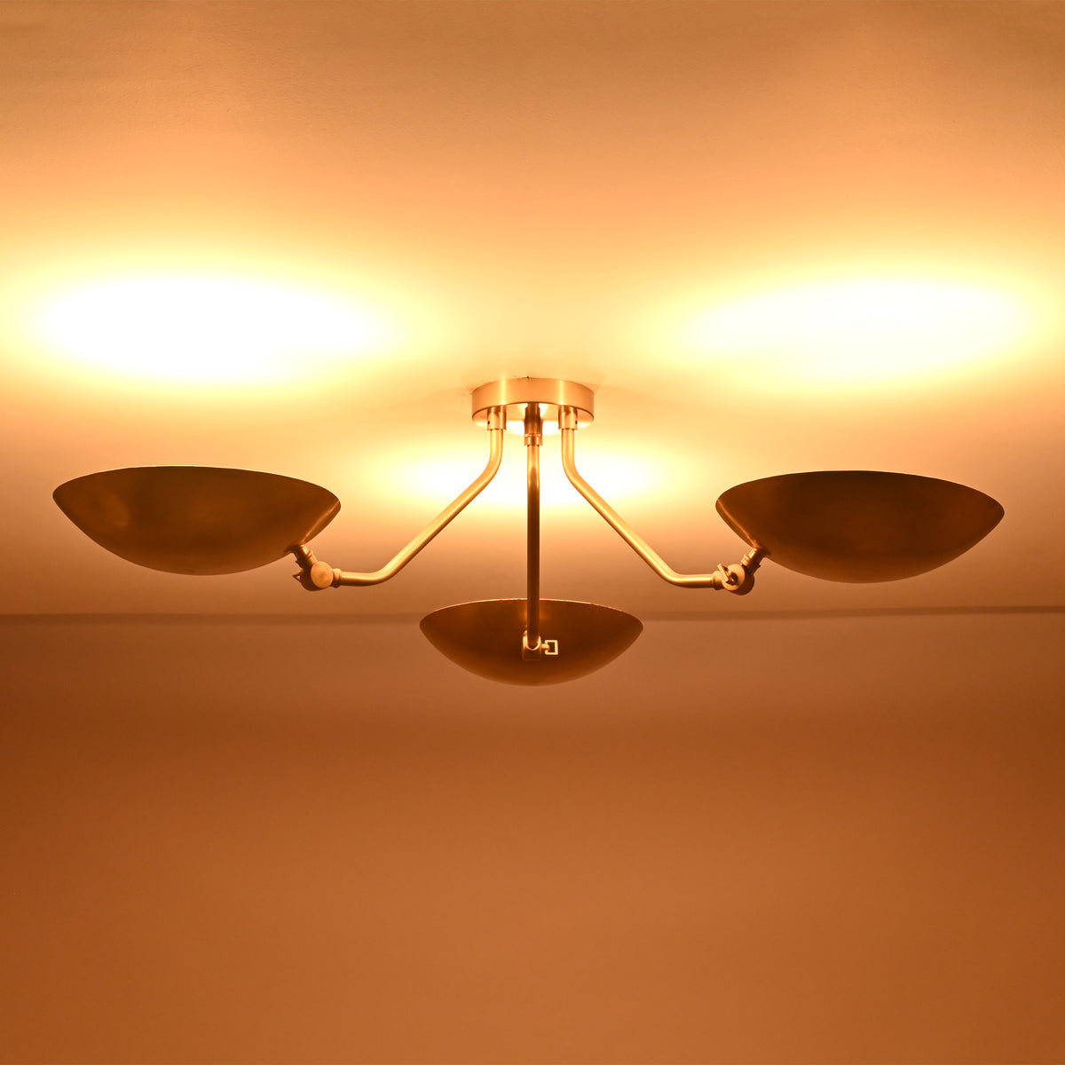 Wide illuminated view of Hudson Mid-Century Modern triple dish chandelier casting warm indirect ambient light.