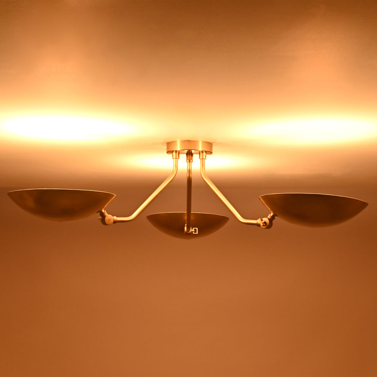 Illuminated front view of Hudson triple dish chandelier creating warm indirect ambient ceiling lighting.