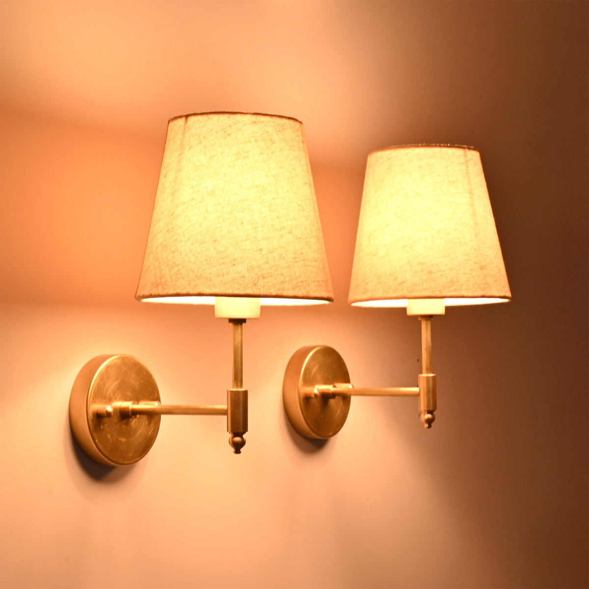 Angled illuminated view of the Milan natural linen shade brushed brass wall sconces showcasing soft warm lighting.