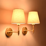 Angled illuminated view of the Milan natural linen shade brushed brass wall sconces showcasing soft warm lighting.