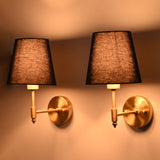 Warm-lit antique brass wall sconce with a rich blue tapered fabric shade shown from an angled perspective, highlighting its elegant profile.