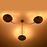 Bottom view of a brass flushmount chandelier with three bowl-shaped shades, warmly illuminating the ceiling.