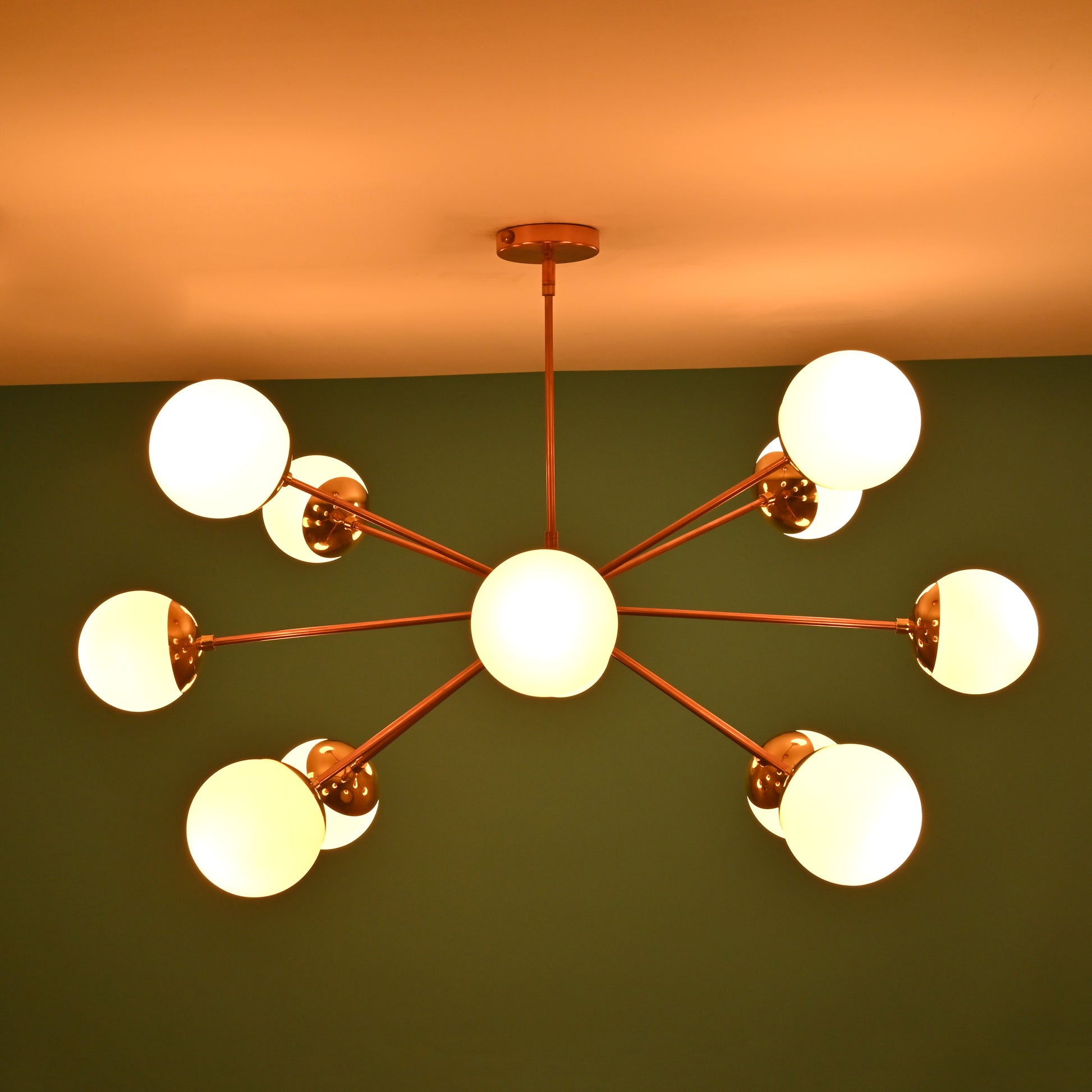 Side view of a lit brass Sputnik chandelier with frosted globe shades, set against a green wall background.