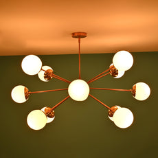 Side view of a lit brass Sputnik chandelier with frosted globe shades, set against a green wall background.