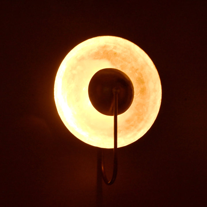 Brass wall sconce glowing warmly in the dark, round shade with radiant halo ambient effect