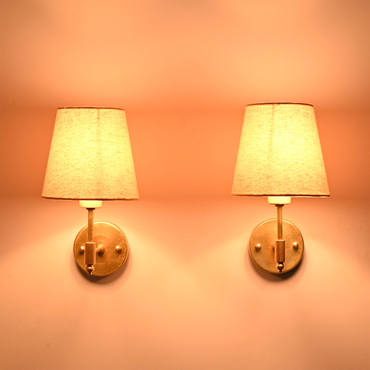 Illuminated Milan brushed brass wall sconces with natural linen fabric shades creating a warm ambient glow.