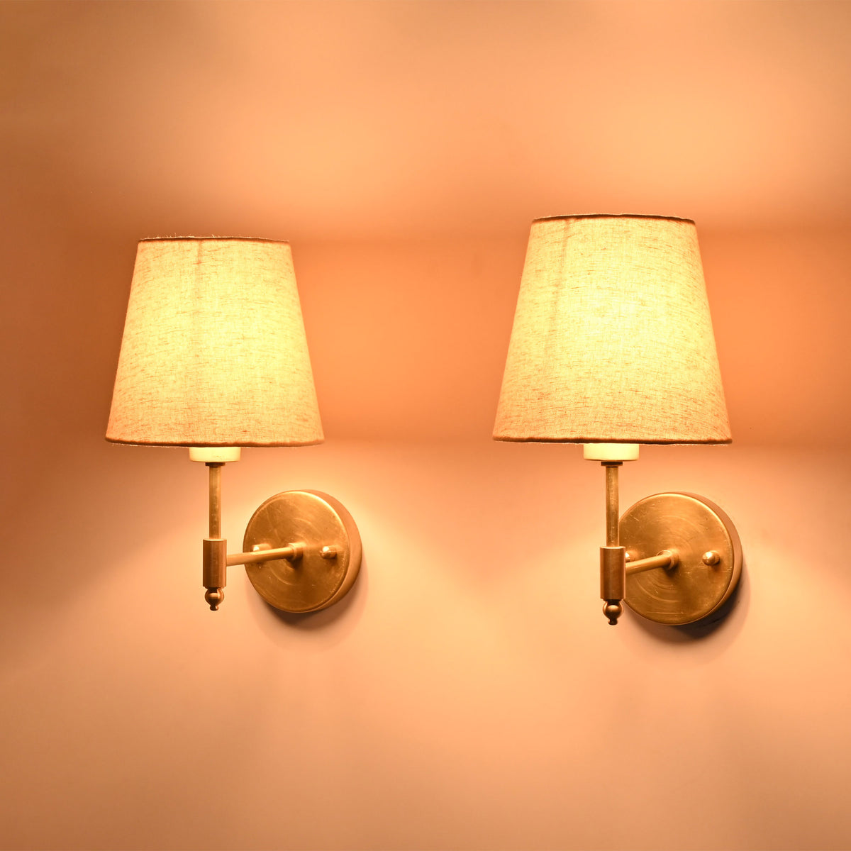 Side perspective of the illuminated Milan brushed brass wall sconces with natural linen tapered fabric shades.