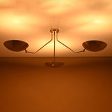 Three-arm brushed brass ceiling light glowing warmly, showing indirect ambient lighting from bowl shades