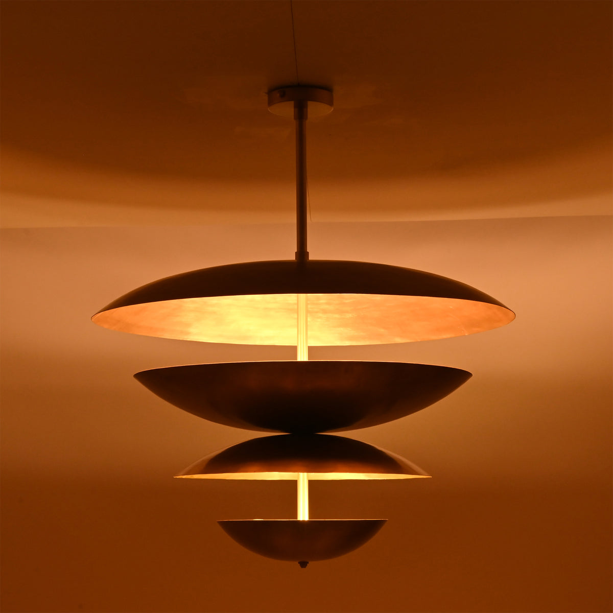 Warm illuminated detail of the Lior Modern Tiered Disc Chandelier emphasizing layered metal discs and architectural lighting effect