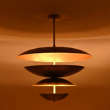 Warm illuminated detail of the Lior Modern Tiered Disc Chandelier emphasizing layered metal discs and architectural lighting effect