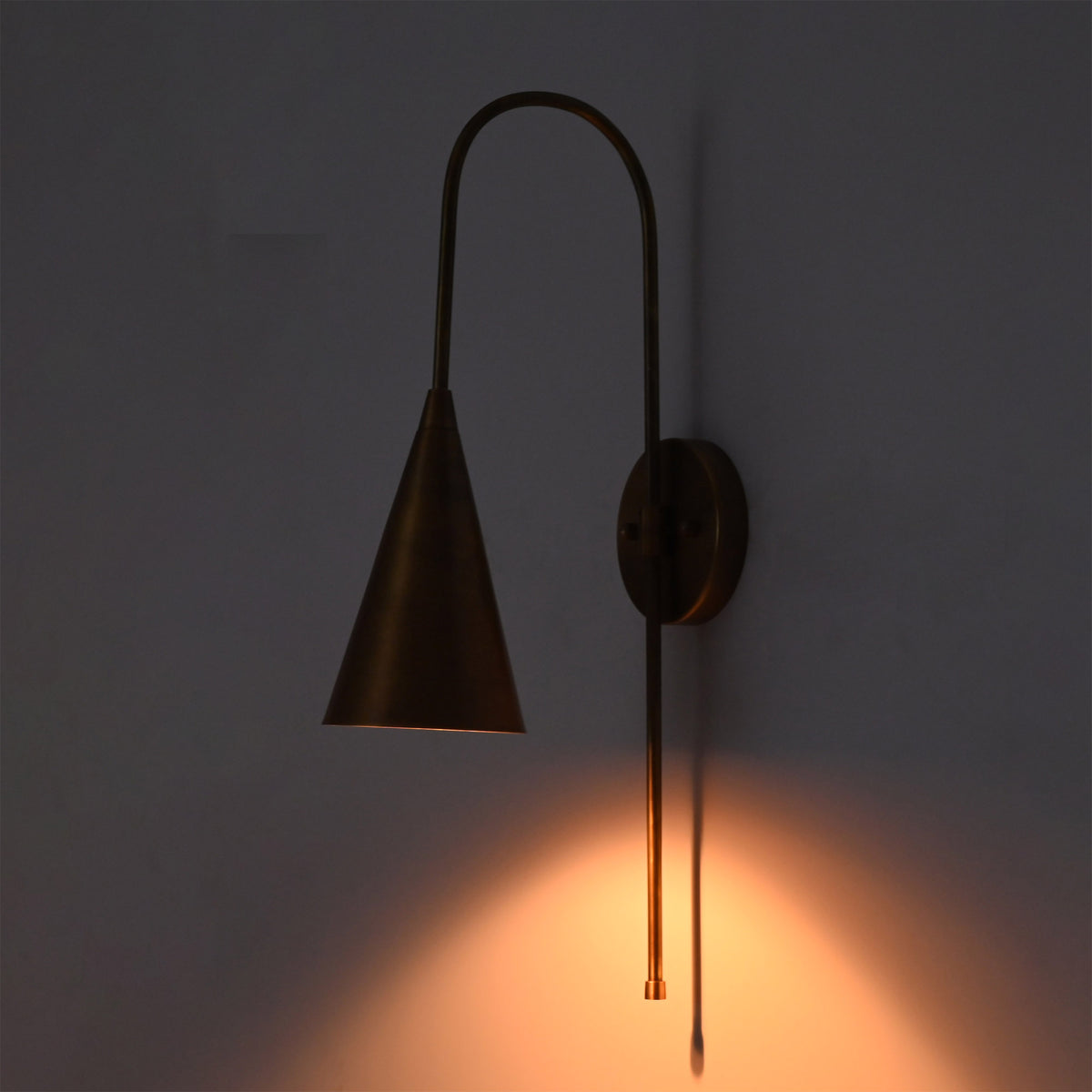 Close front view of Liora Cone Loop Wall Sconce showing focused warm light from the tapered cone shade.
