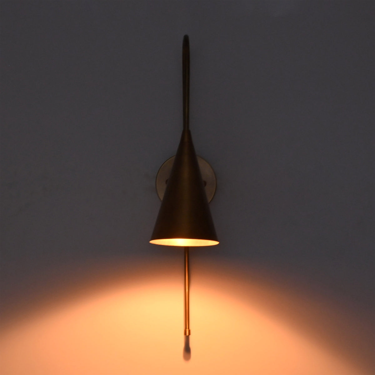 Liora Cone Loop Wall Sconce displayed in low light with a soft amber glow beneath the cone shade.