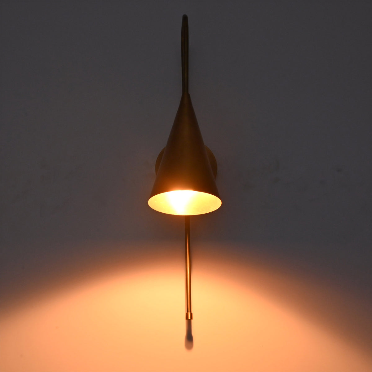 Liora Cone Loop Wall Sconce displayed in low light with a soft amber glow beneath the cone shade.