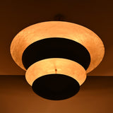 Illuminated chandelier with layered black and gold dome discs, casting a warm ambient light and dramatic shadows, creating a striking sculptural centerpiece on the ceiling.