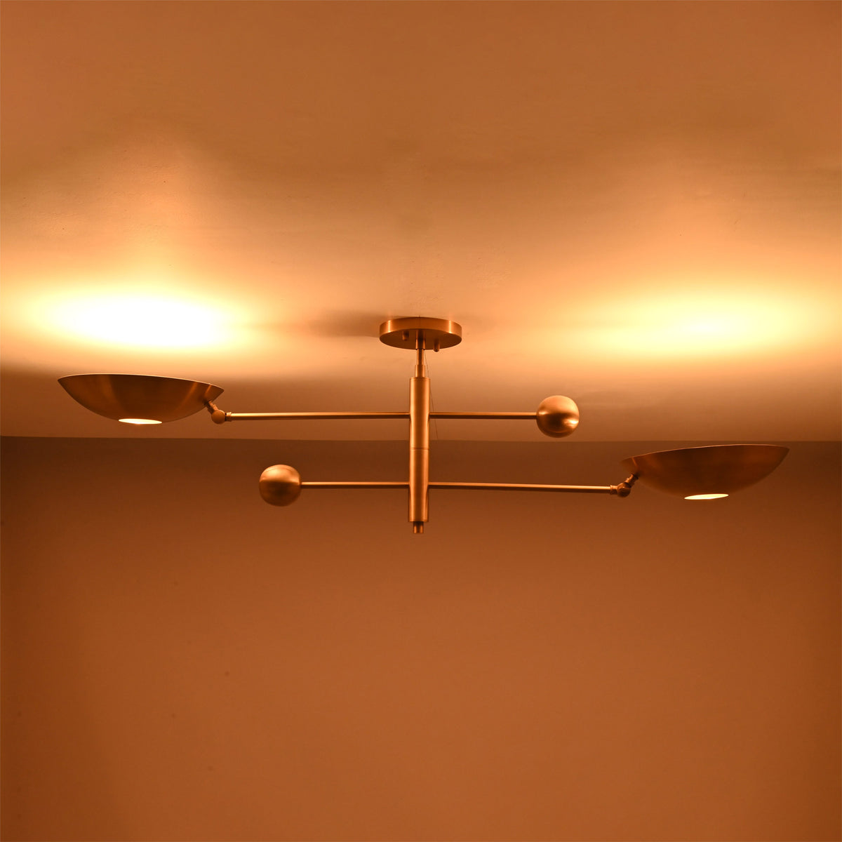 Warm illuminated detail of the Luna Modern Double Bowl Chandelier highlighting its sculptural brass bowl shades and balanced linear design
