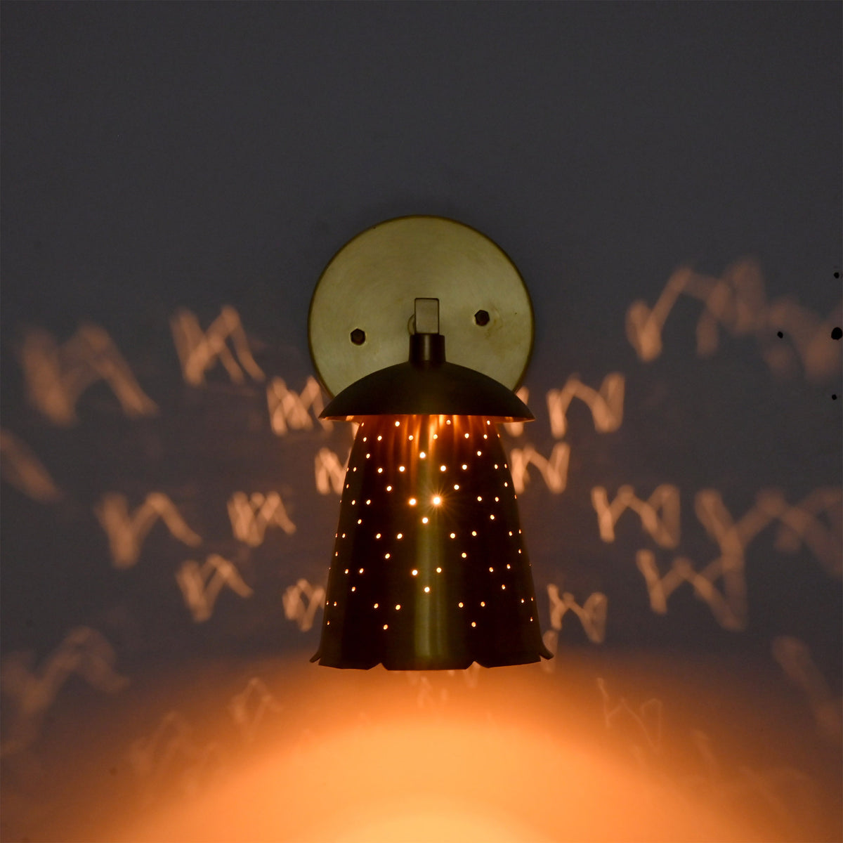 : Luna perforated bell wall sconce glowing warmly with dotted light patterns across the surrounding wall.