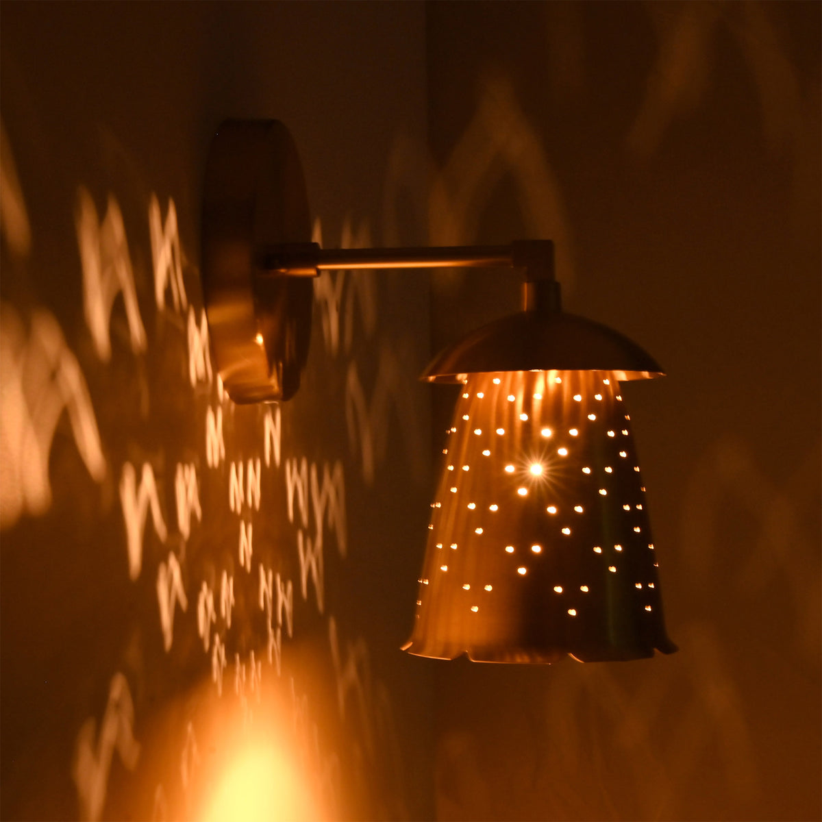 Side view of illuminated Luna perforated bell wall sconce casting warm patterned light on the wall.