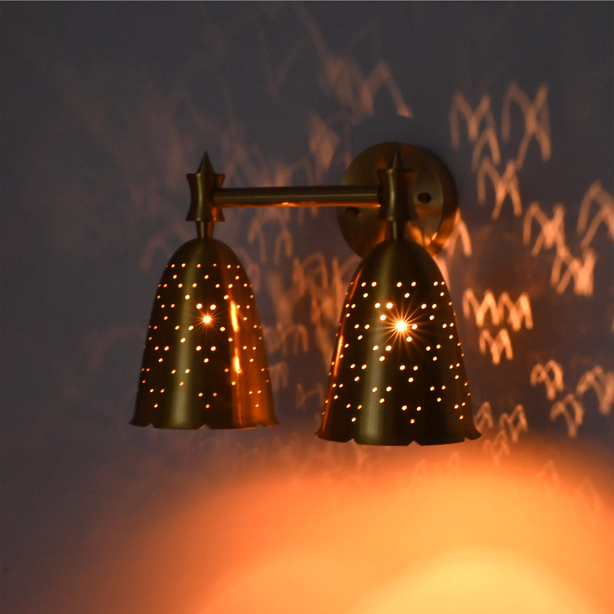 Angled illuminated double bell wall sconce creating decorative dotted light patterns and warm ambient glow.