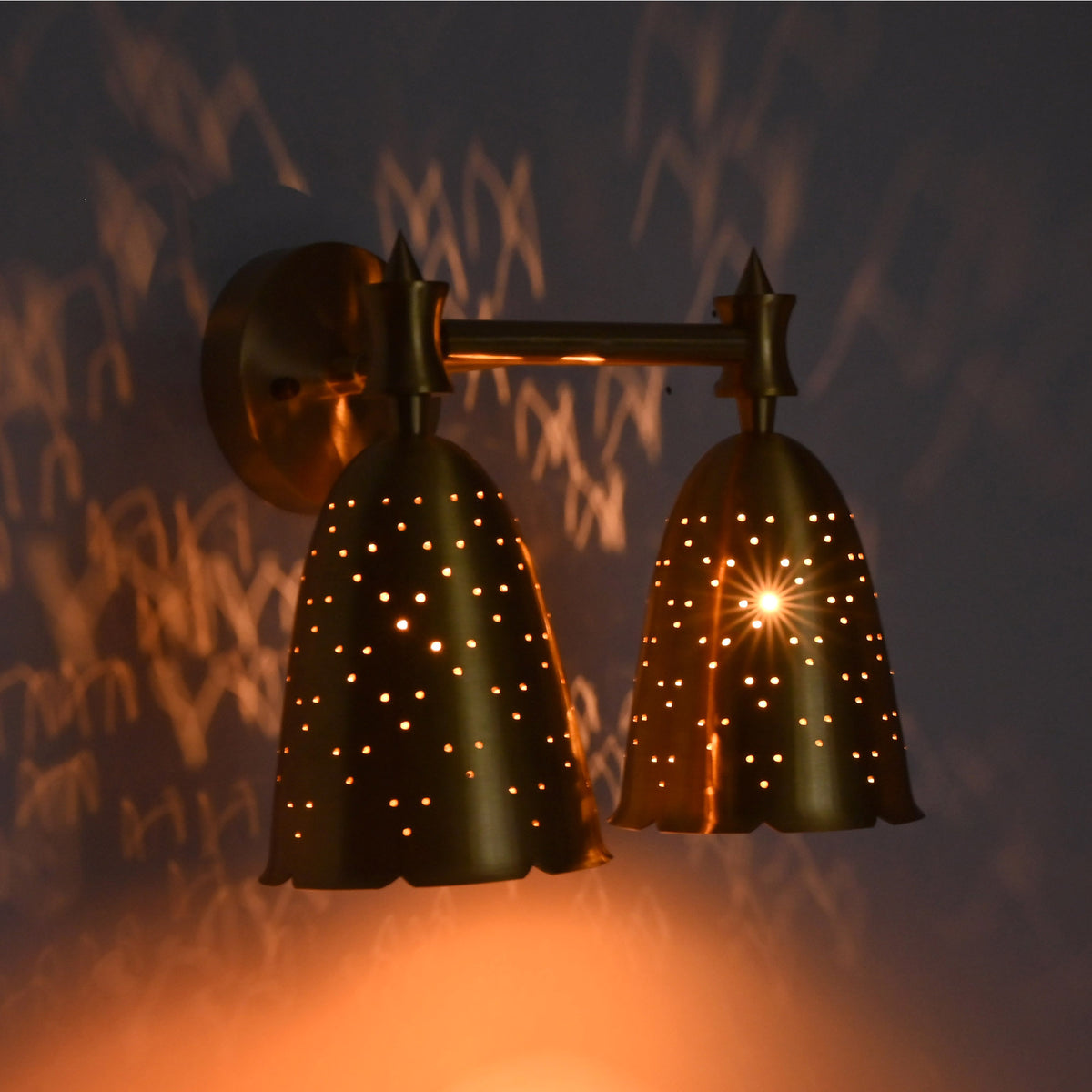 Close view of twin perforated bell shades glowing warmly with star-like light effects and patterned shadows.